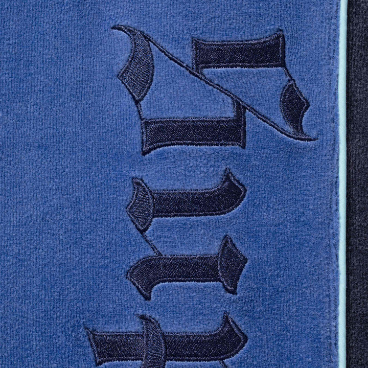 Close-up of the navy blackletter Supreme embroidery on the blue velour track pants