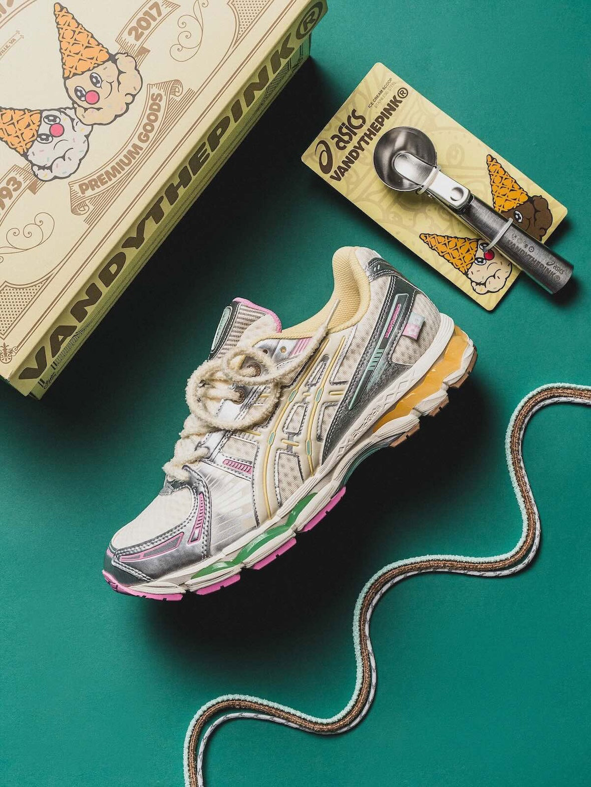 Vandy The Pink Asics Gel-Kayano 12.1 Vanilla, one shoe on green beside the printed box, a branded ice cream scoop and a spare lace