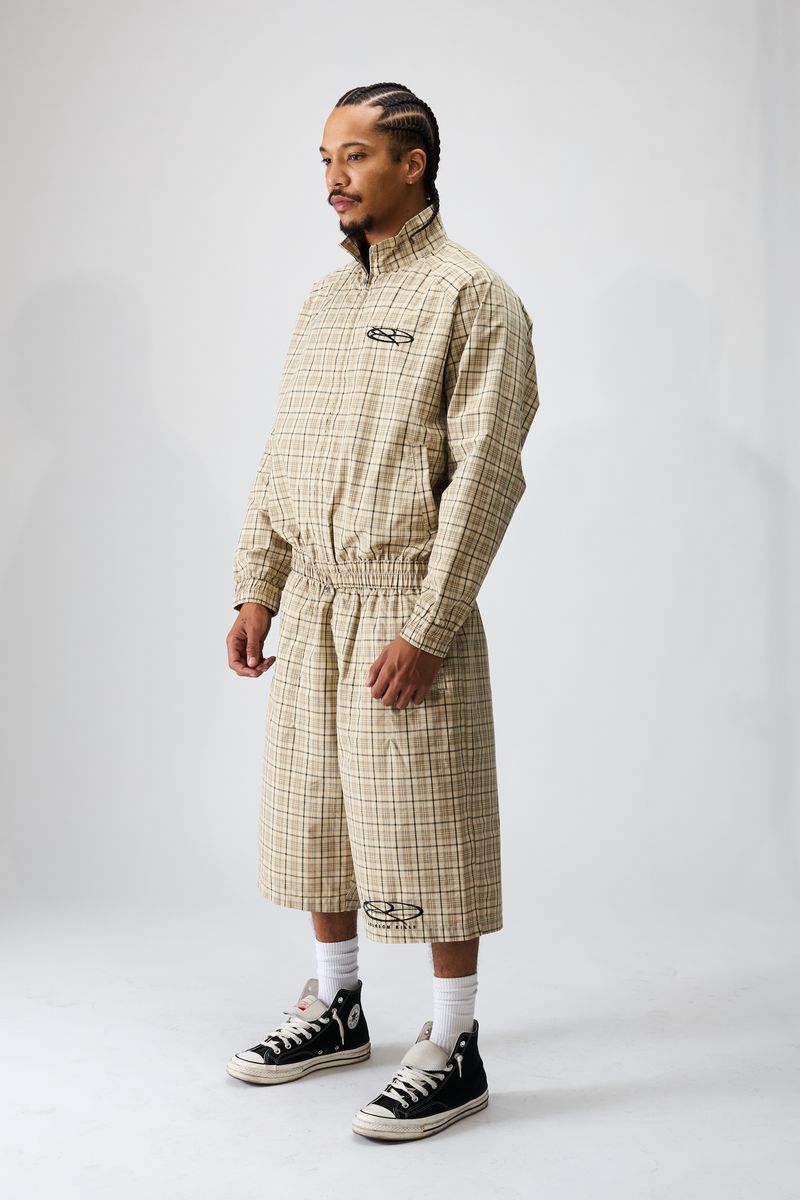 Boredom Kills Khaki Plaid Track Shorts on a model in the full khaki set, three-quarter turn