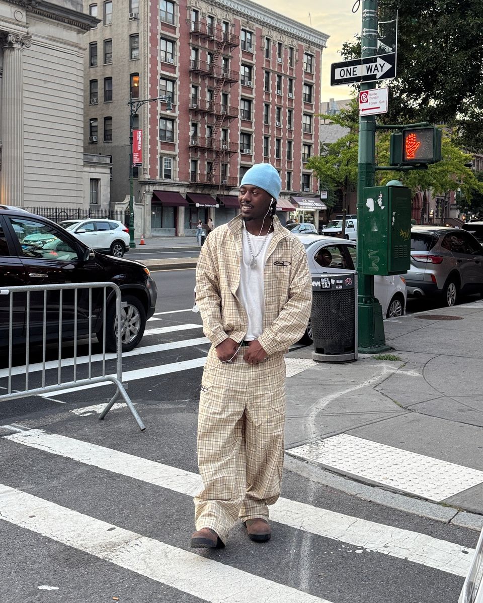 Boredom Kills Khaki Plaid Track Pants on a model crossing a New York street in the full set and a blue beanie