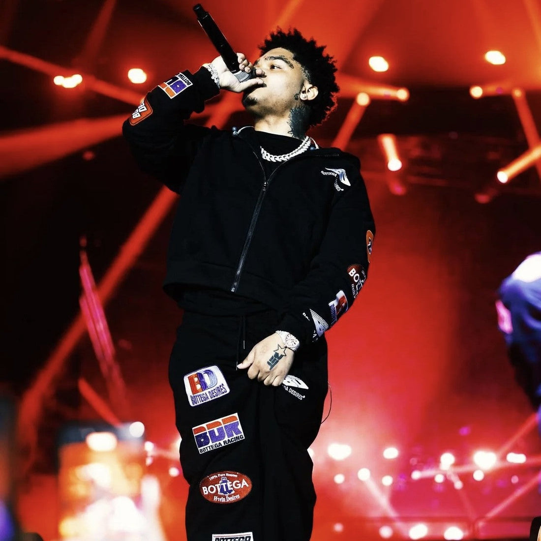Performer on stage under red lights wearing the Bottega Desires black patched zip hoodie and matching pants