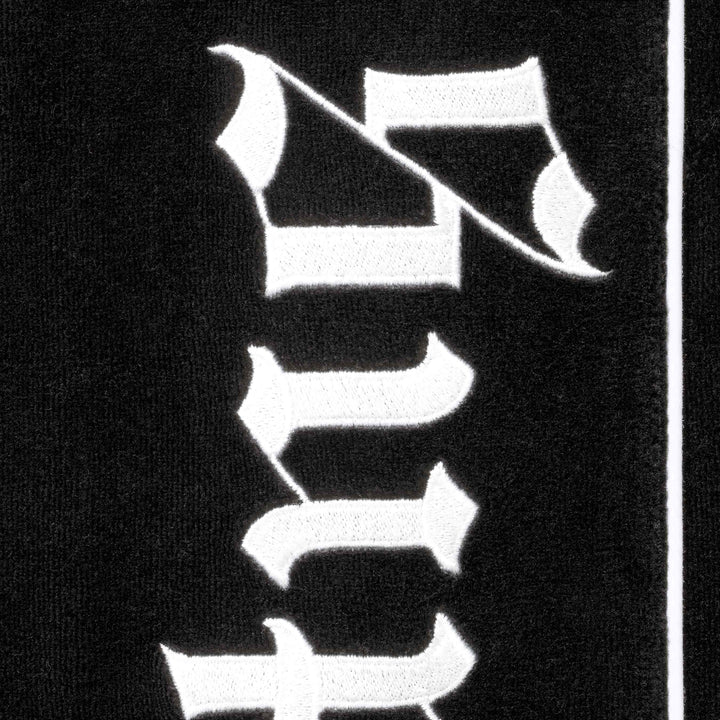 Close-up of the white blackletter Supreme embroidery on the black velour track pants
