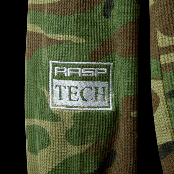 Close-up of the white RASP TECH embroidered patch on green camo waffle knit