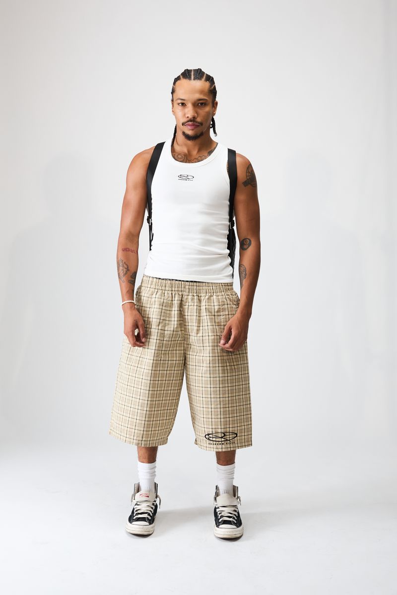Boredom Kills Khaki Plaid Track Shorts on a studio model with a white tank and black and white low-top sneakers