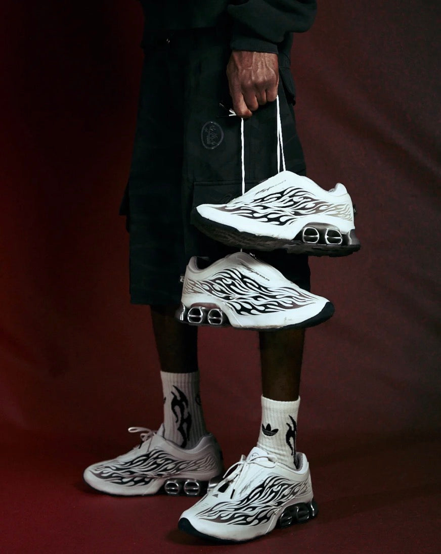 Hellstar Adidas Megaride White, model wearing the pair with flame-print socks and black cargo shorts, holding a second pair by the laces