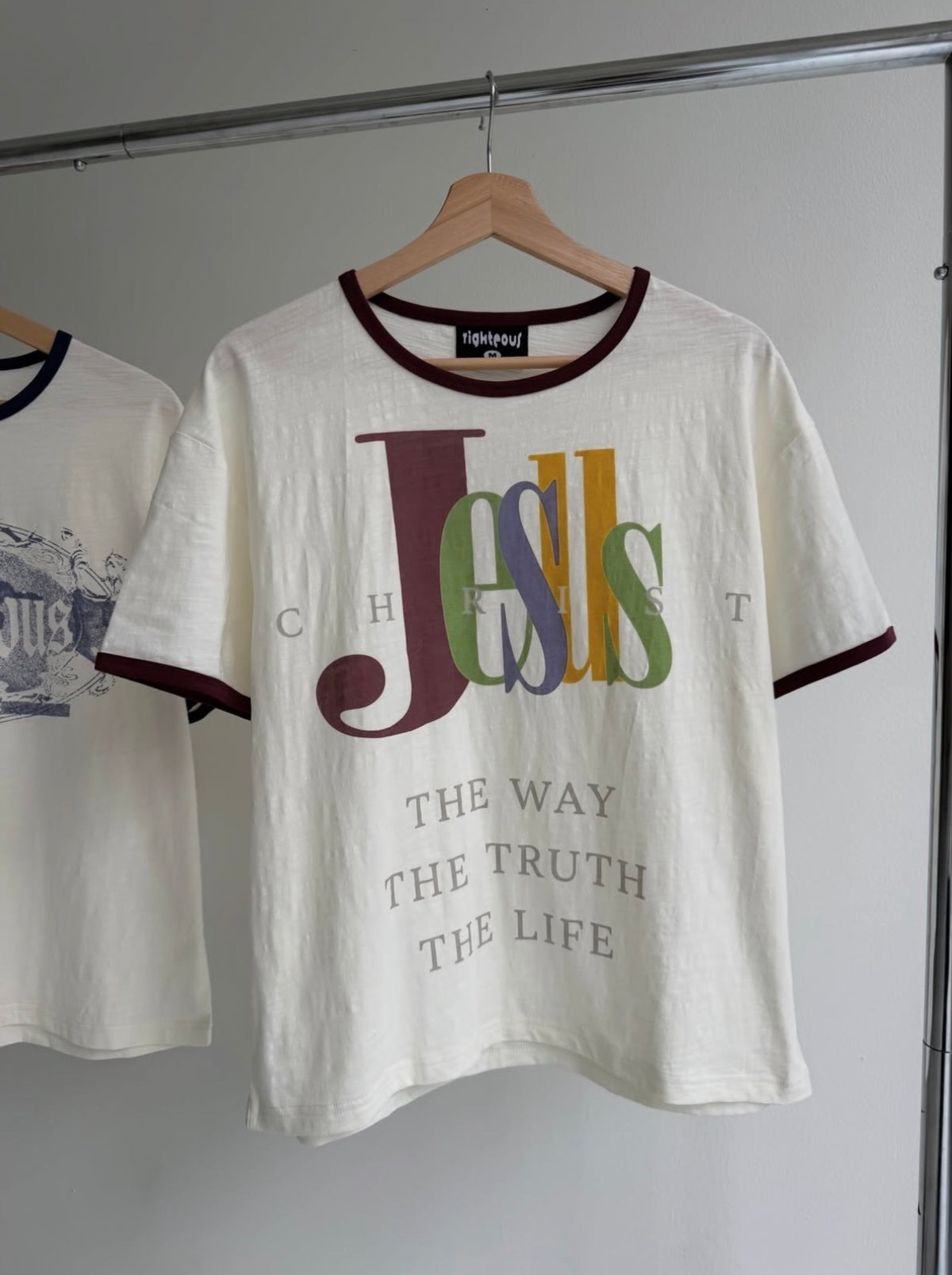 We Are Righteous The Truth Ringer Tee on a wooden hanger showing the front wordmark