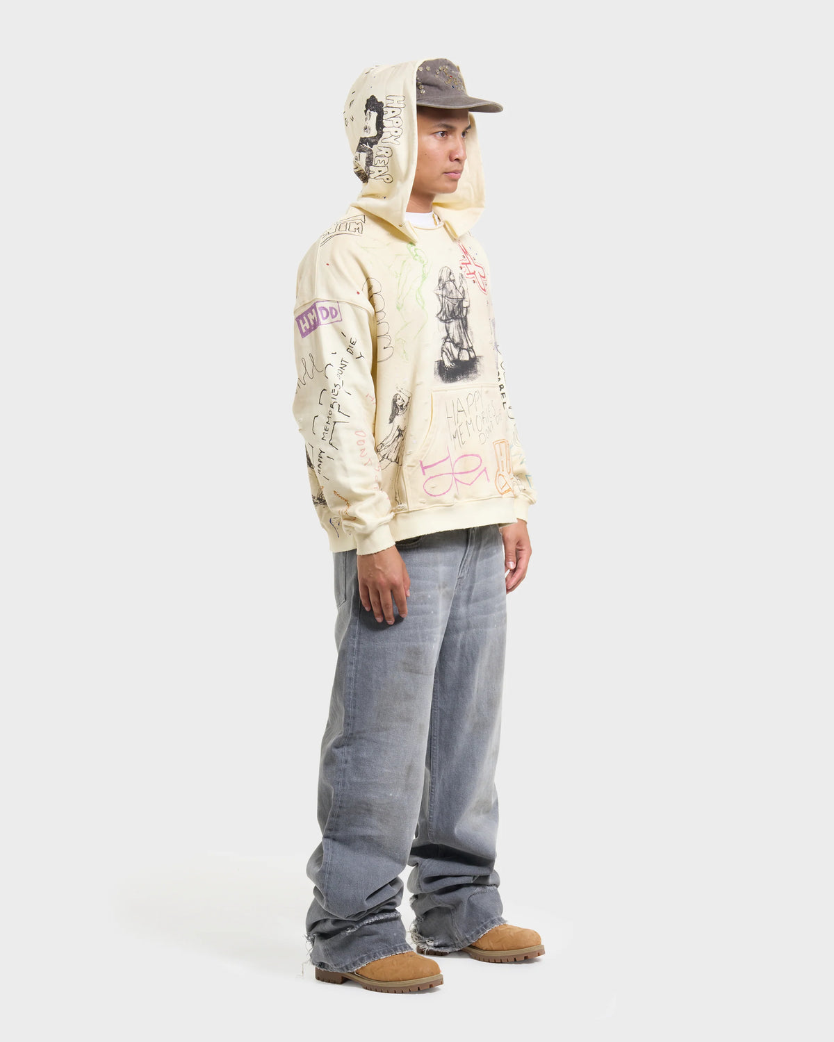 HMDD Sketch Hoodie, full-length model in a cap wearing the sketch-covered hoodie with baggy grey jeans and brown boots