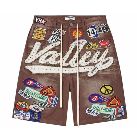 Front of the Vale Brown 1980s Jorts in washed brown denim, covered with Valley Dreams patches and a white chainstitched Valley script down the leg