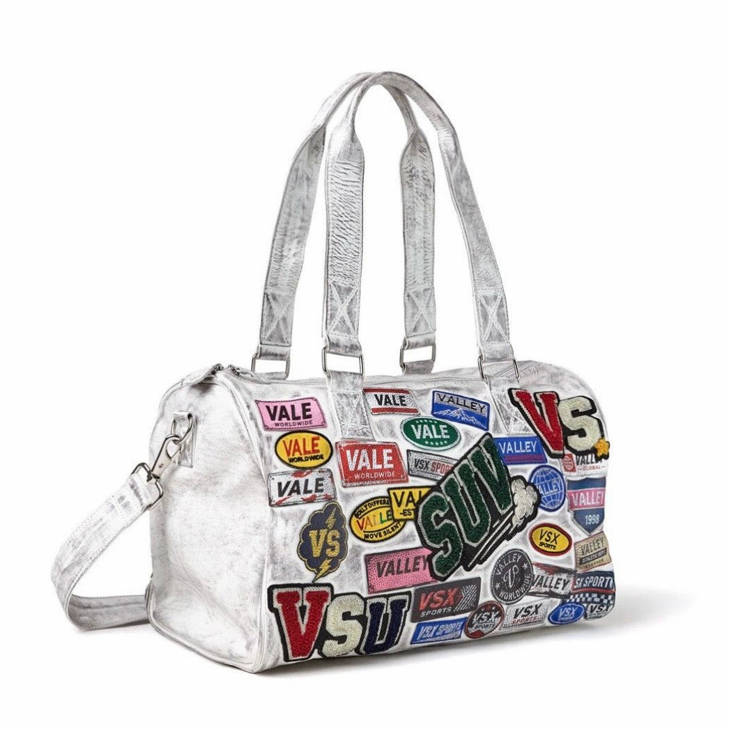 Vale Airport Duffle 1/100, white duffle bag covered in printed Vale and VS patch graphics, with handles and a shoulder strap