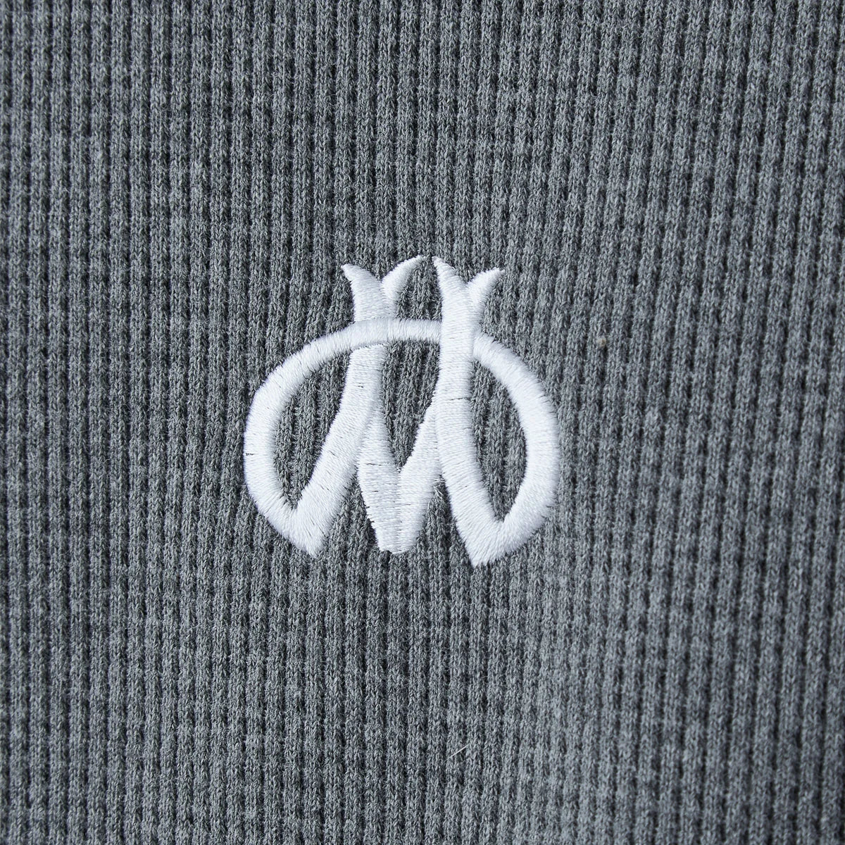 Close-up of the white embroidered winged monogram on grey waffle thermal knit