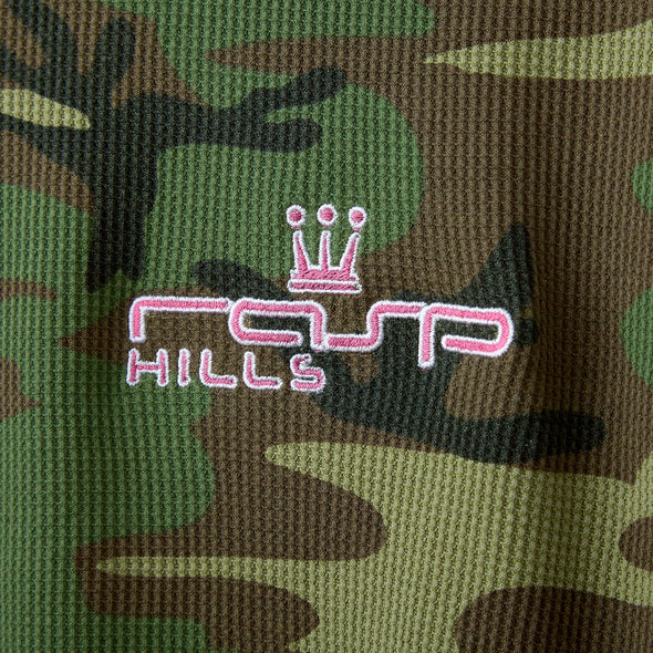 Close-up of the pink crowned RASP HILLS embroidery on green camo waffle knit
