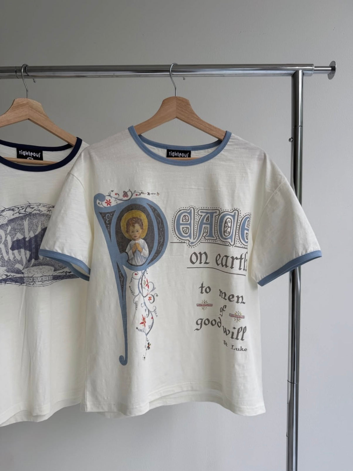 We Are Righteous Peace On Earth Ringer Tee on a wooden hanger on a chrome rail