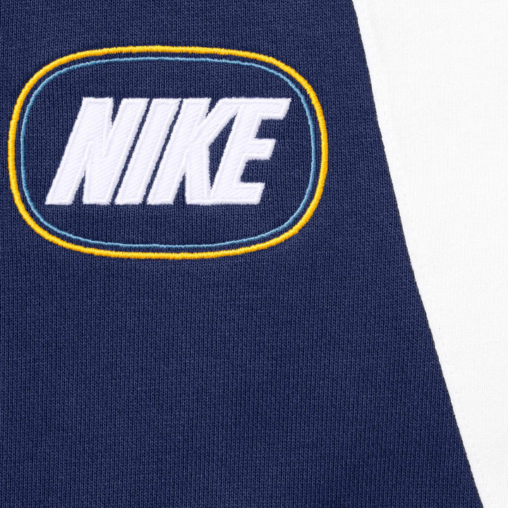 Close-up of the NIKE oval logo in light blue and gold on the navy sweatpants