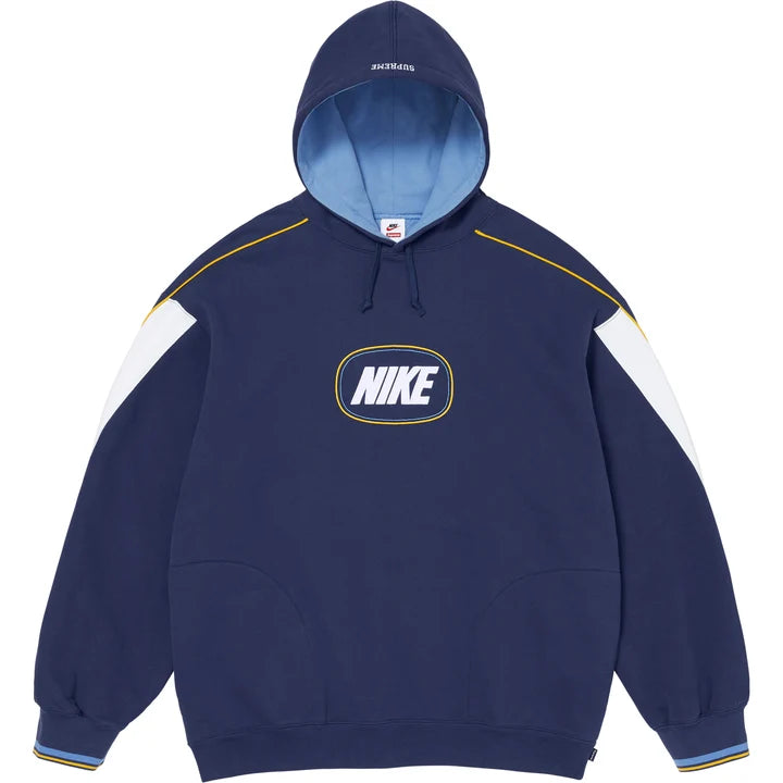 Supreme x Nike hoodie in navy with curved white shoulder panels, gold piping, light blue hood lining and an oval NIKE logo on the chest, front view