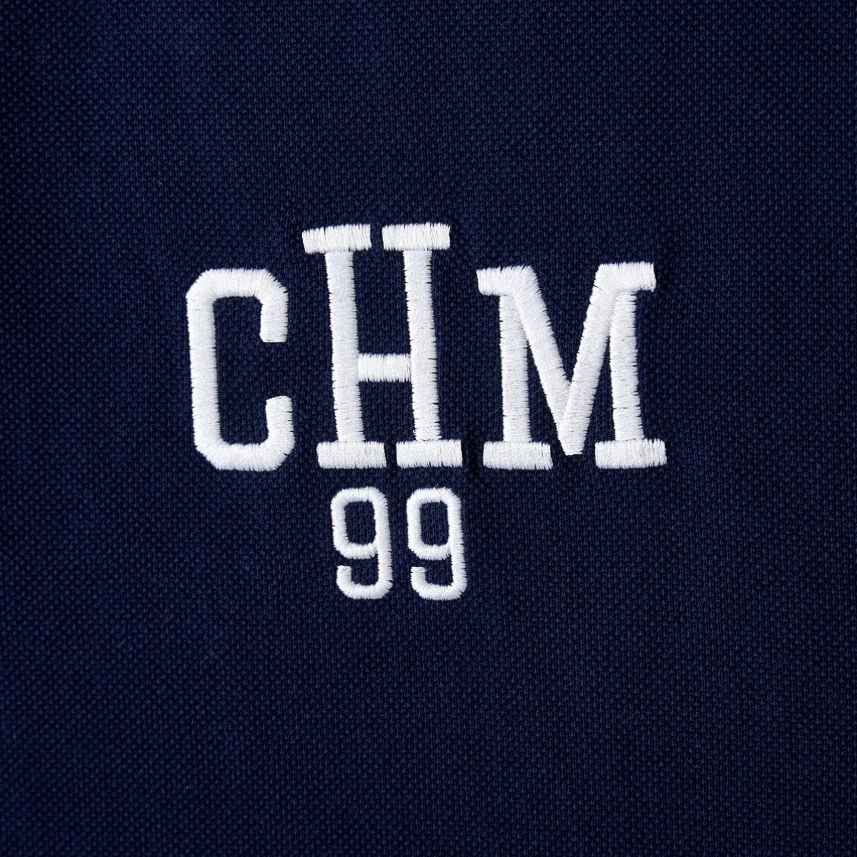 HMDD Glo Navy Polo, close-up of the white CHM 99 embroidery on the navy pique fabric