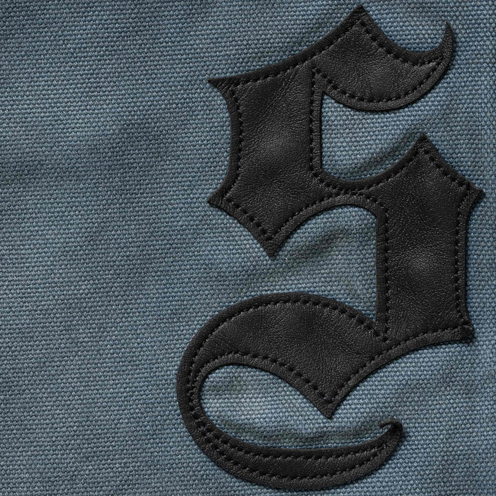 Close-up of the black leather blackletter applique stitched onto the washed blue painter pants