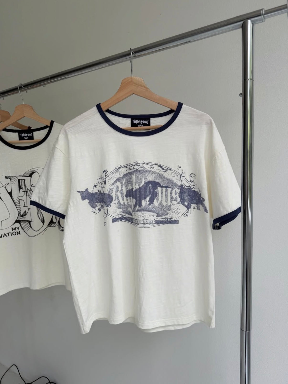 We Are Righteous Holy Sacrifice Ringer Tee hanging on a garment rack with the front graphic visible