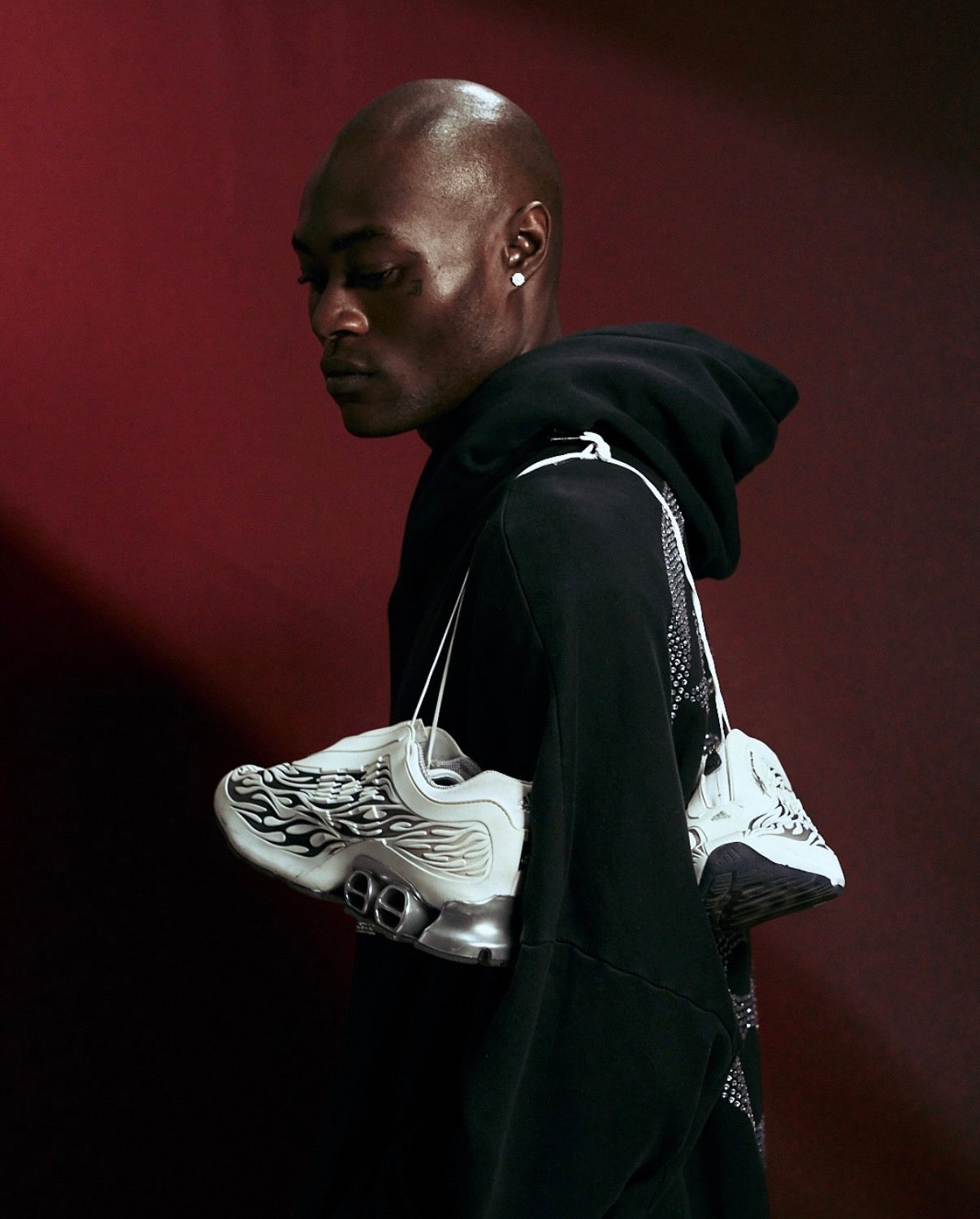 Hellstar Adidas Megaride White, side profile of a model in a black hoodie holding the white sneakers up by their laces