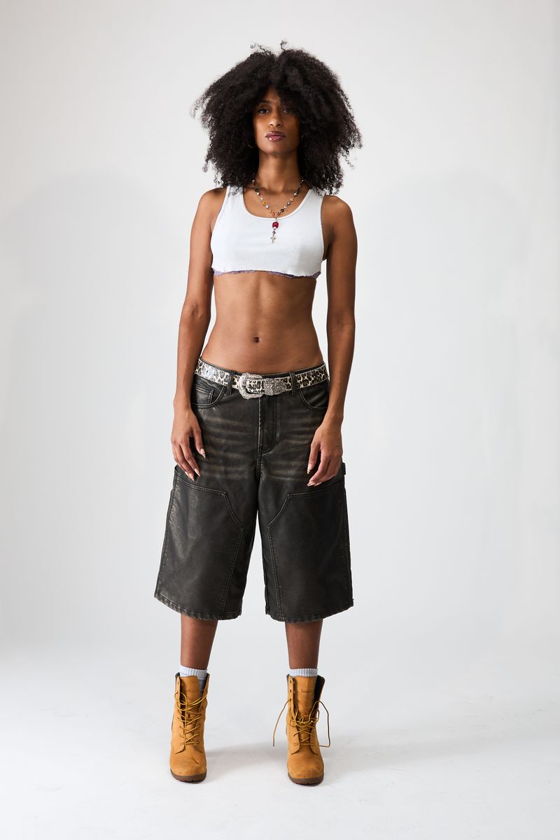 Boredom Kills Black Leather Shorts, model in the faded knee-length shorts with a white bra top and studded belt