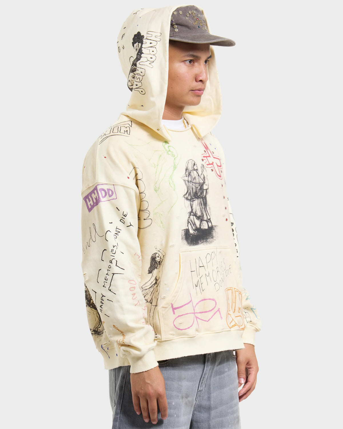 HMDD Sketch Hoodie, side profile of the model with the hood up under a cap, sketch-covered cream fleece over grey jeans