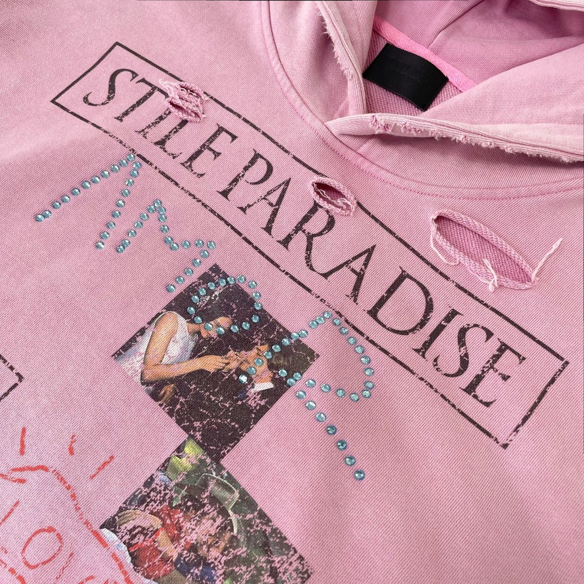 Close-up of the boxed STILE PARADISE chest print and distressed holes on the pink hoodie