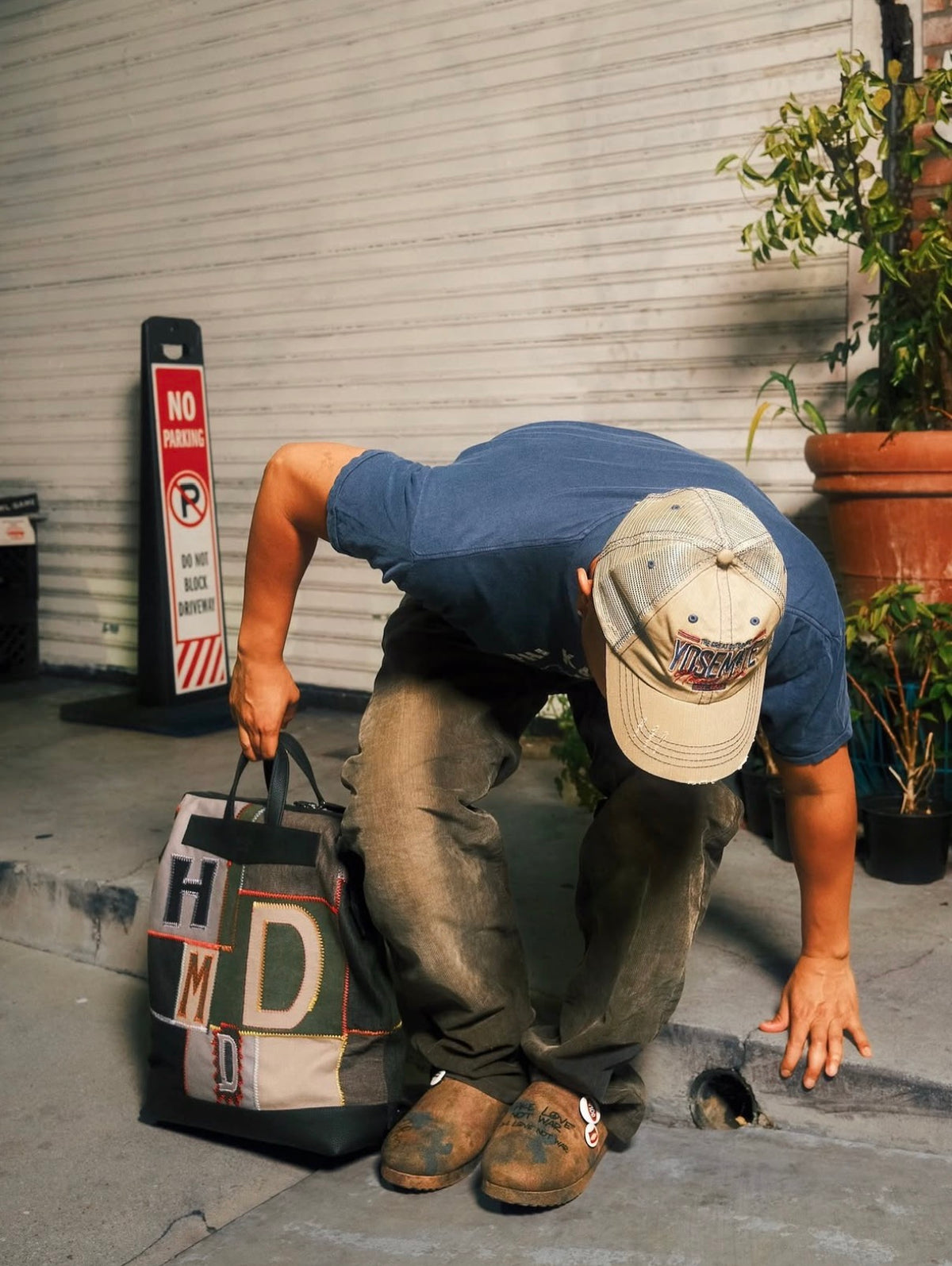 Model carrying the HMDD Hopscotch Backpack by its top handle, showing the boxy patchwork body