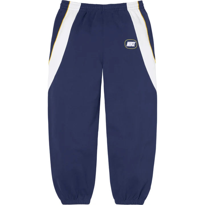 Supreme x Nike paneled sweatpants in navy with curved white side panels and an oval NIKE logo on the thigh, front view