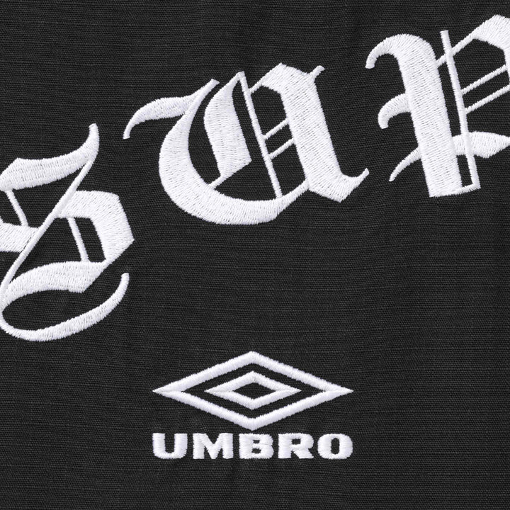 Close-up of white gothic lettering and the Umbro diamond logo embroidered on black ripstop