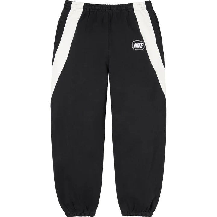 Supreme x Nike paneled sweatpants in black with curved white side panels and an oval NIKE logo on the thigh, front view