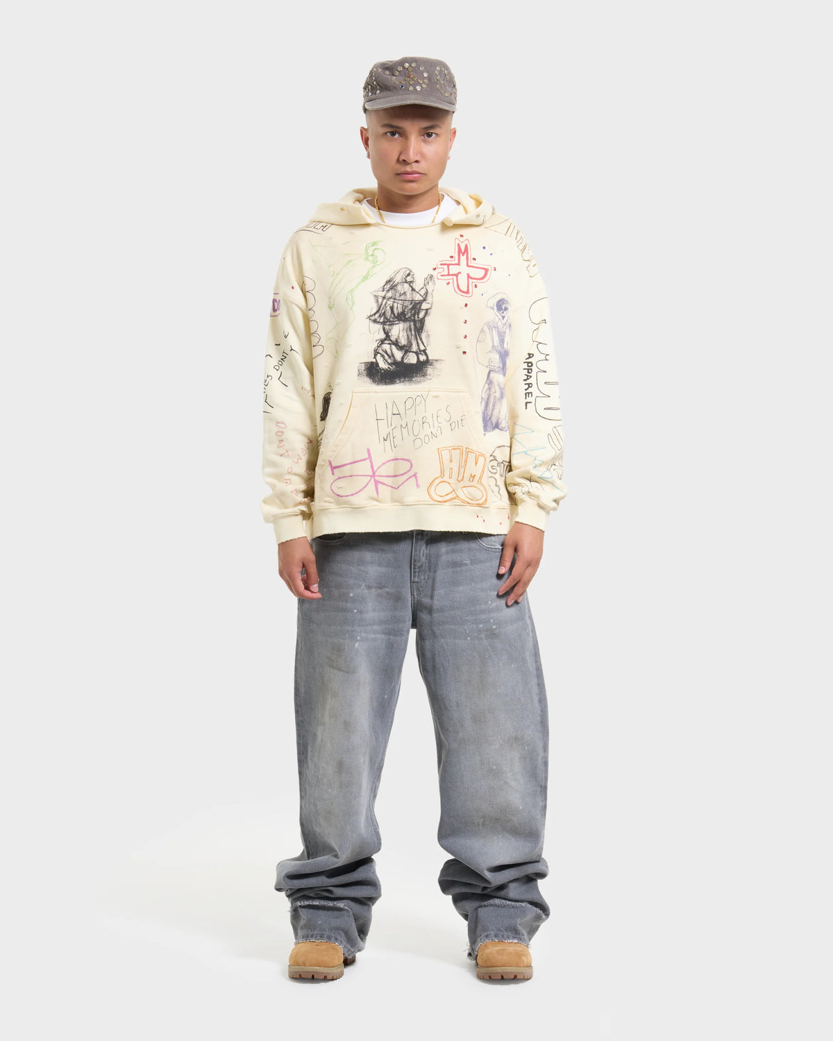 HMDD Sketch Hoodie, model stands facing forward in the cream hoodie over wide grey jeans and brown boots