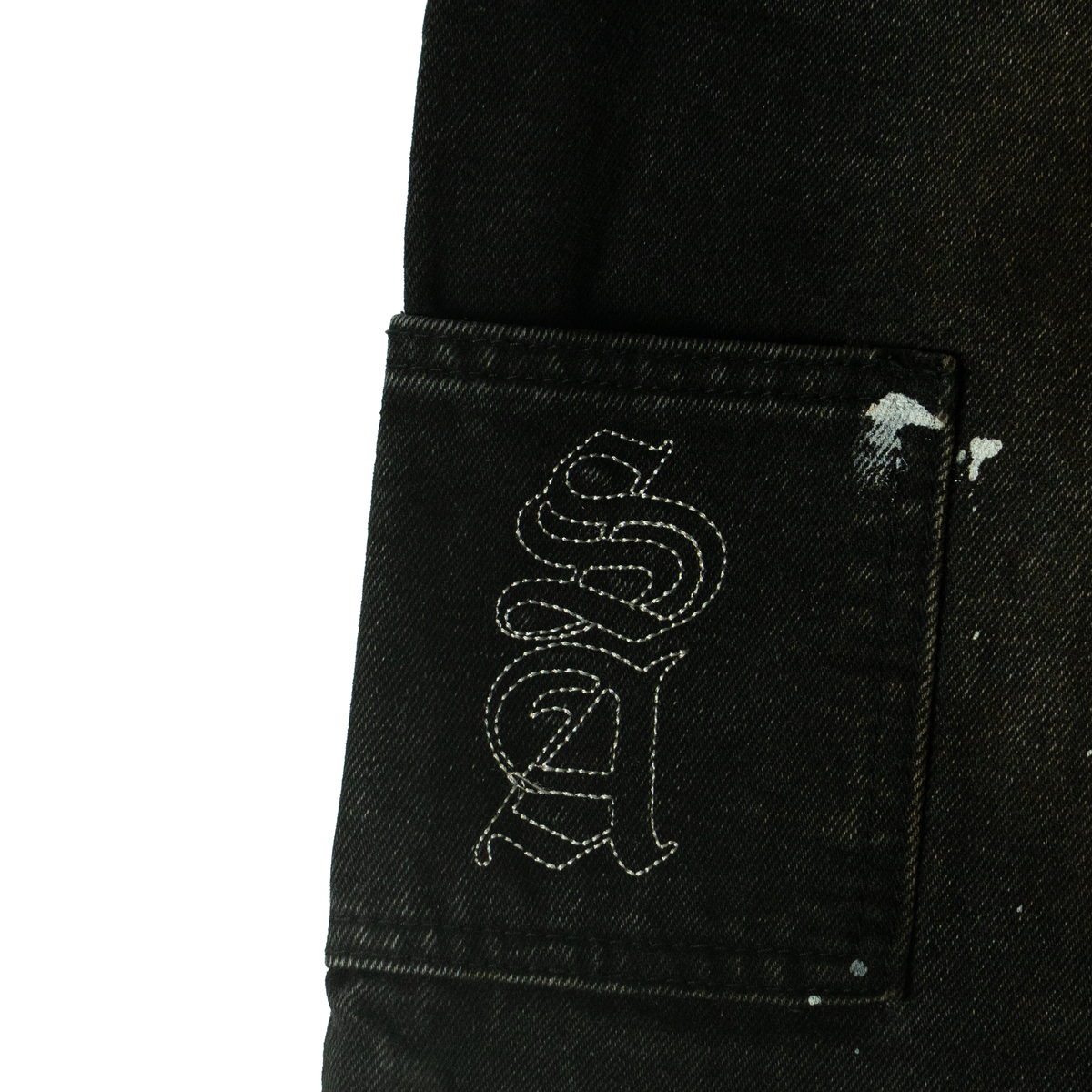 Close-up of the back pocket on the Splatter denim pants with a stitched gothic SA monogram