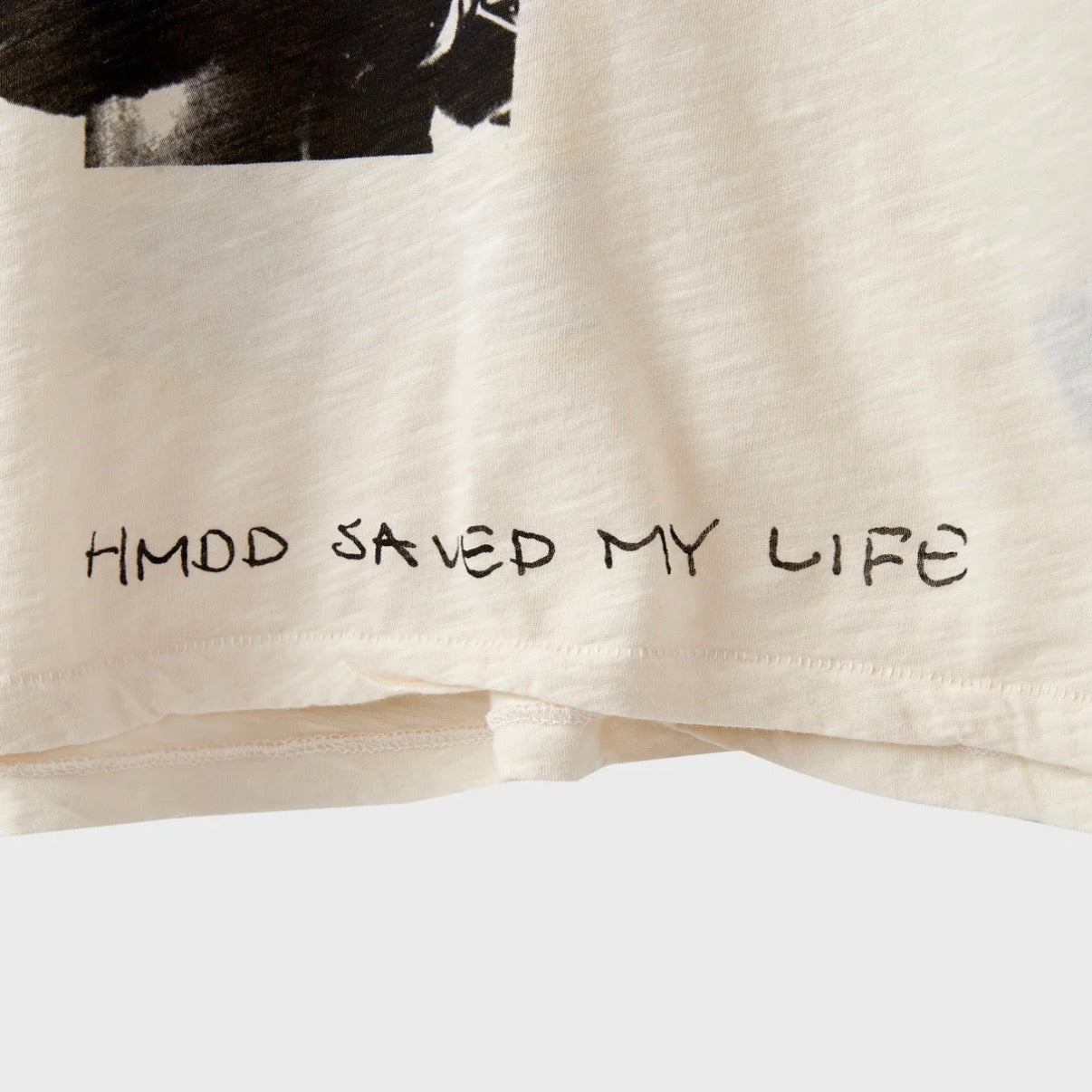 HMDD Boxer Baby Slub T-Shirt, close-up of the lower front hem with HMDD SAVED MY LIFE printed in black on cream slub cotton