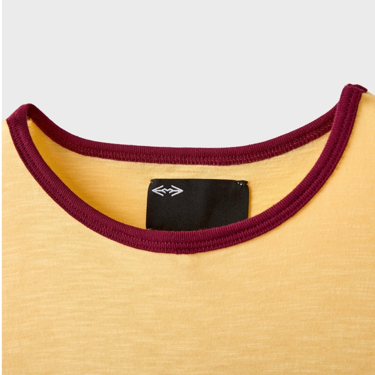 HMDD Stole That T-Shirt, close-up of the burgundy ribbed collar and the black woven neck label on yellow fabric