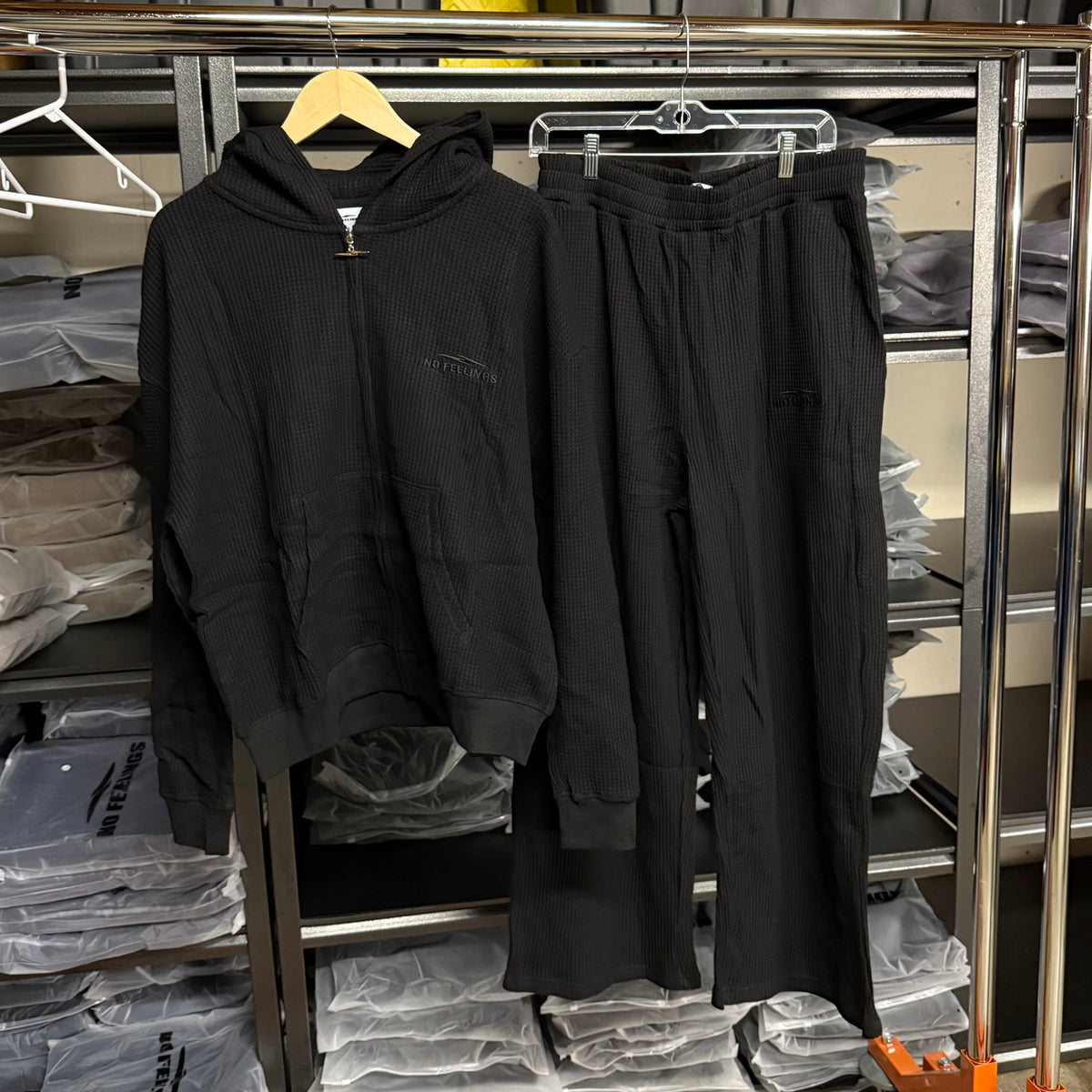 No Feelings black ribbed thermal zip hoodie and matching black sweatpants hanging together on a rack