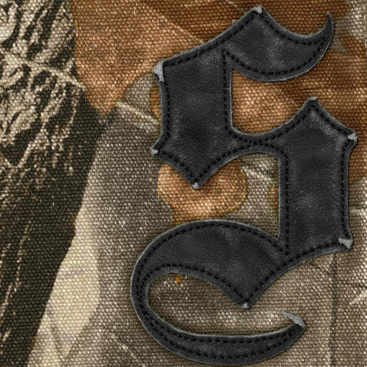 Close-up of the black leather blackletter applique stitched onto the Realtree camo painter pants