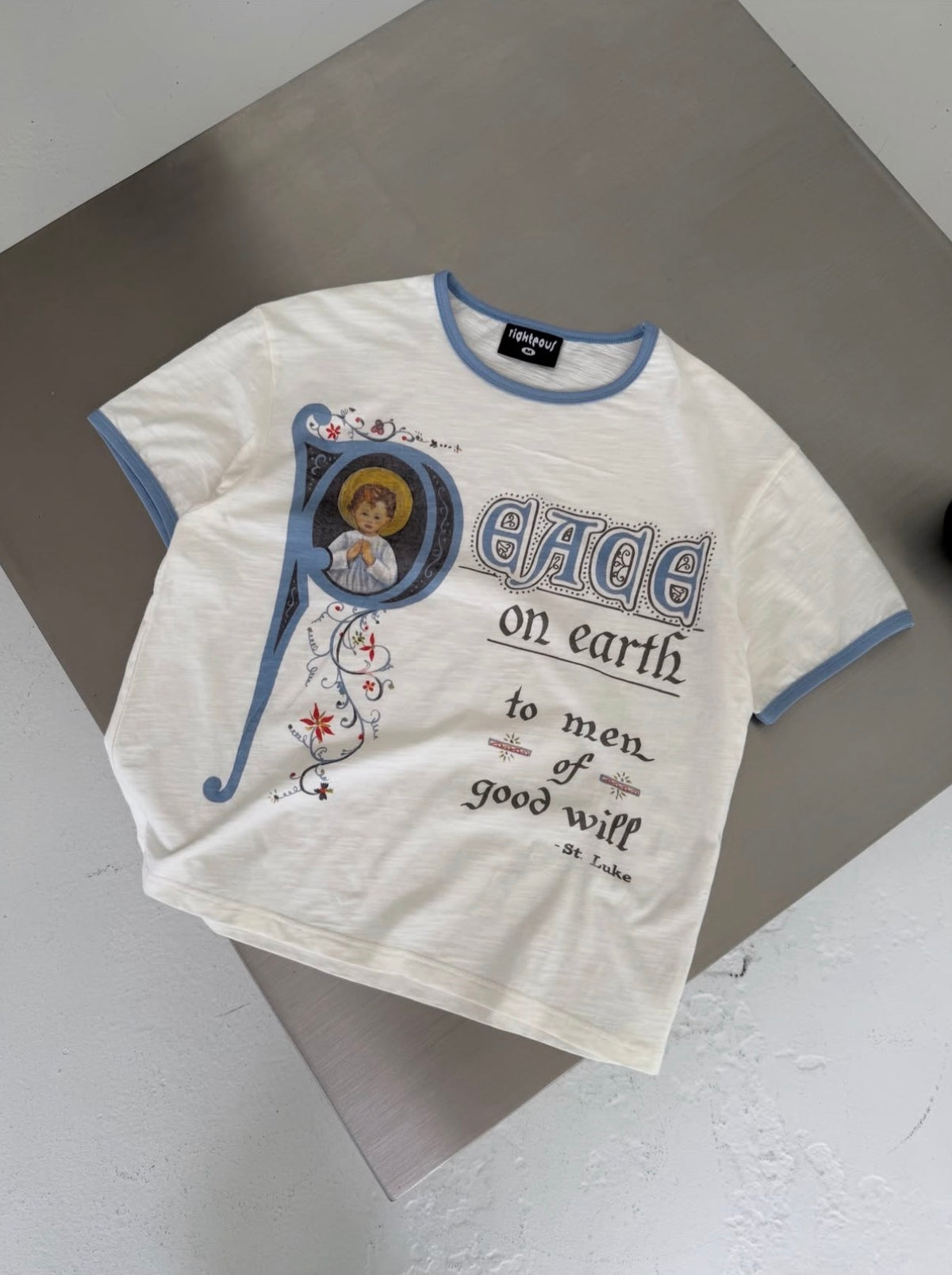 We Are Righteous Peace On Earth Ringer Tee laid flat on a grey plinth and shot from above