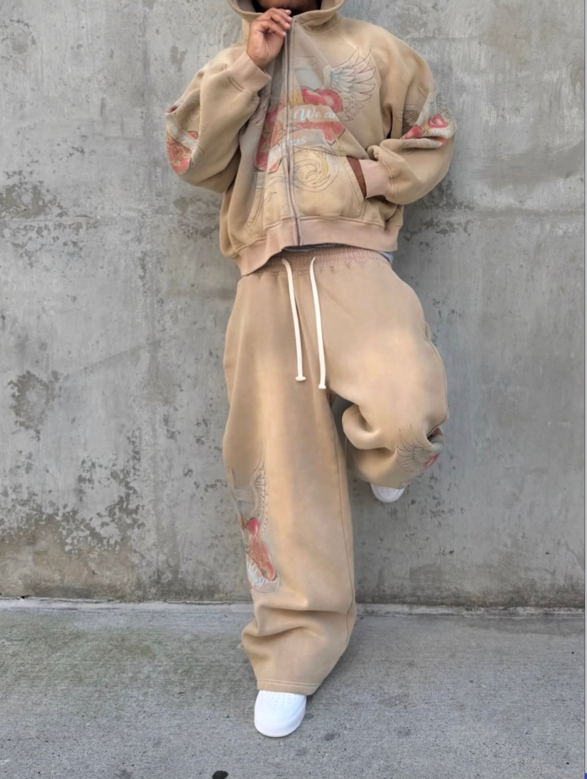 Model in the matching washed tan zip hoodie and sweatpants set by a concrete wall