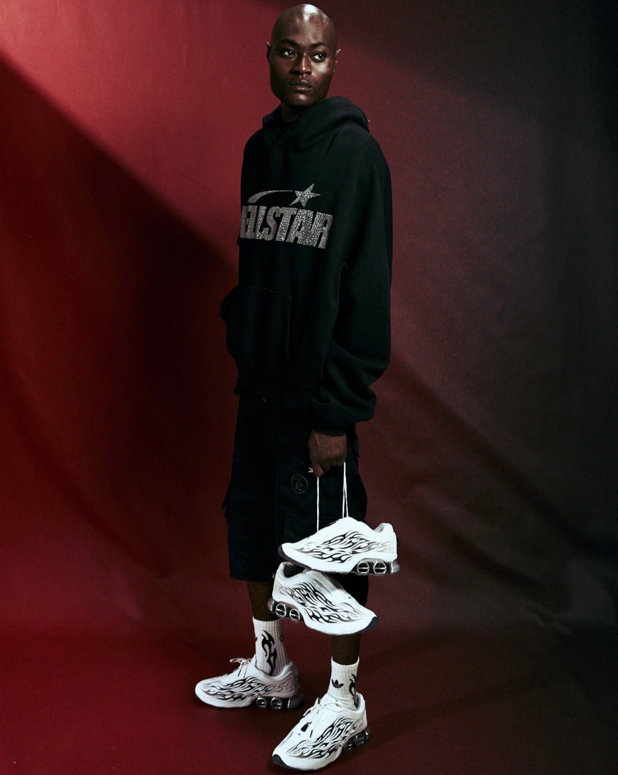 Hellstar Adidas Megaride White, full-length model in black hoodie and black cargo pants holding the sneakers by the laces