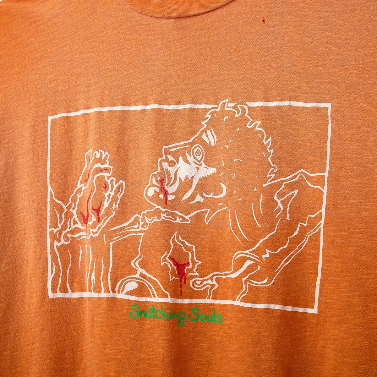 Close-up of the white line-art illustration with red accents on the front of the orange tee