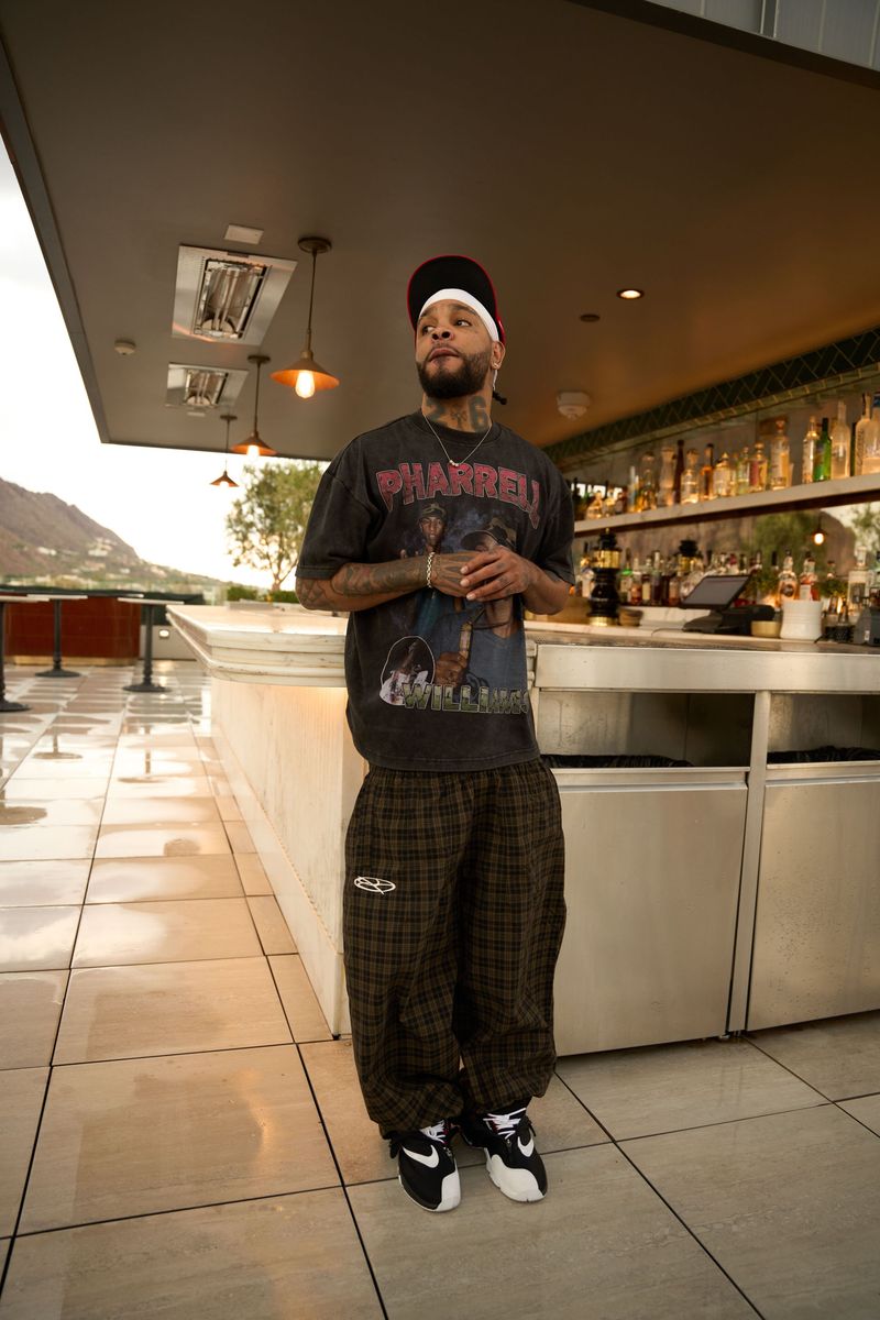 Boredom Kills Black Brown Plaid Track Pants worn in a bar interior with a dark graphic tee, low-angle shot