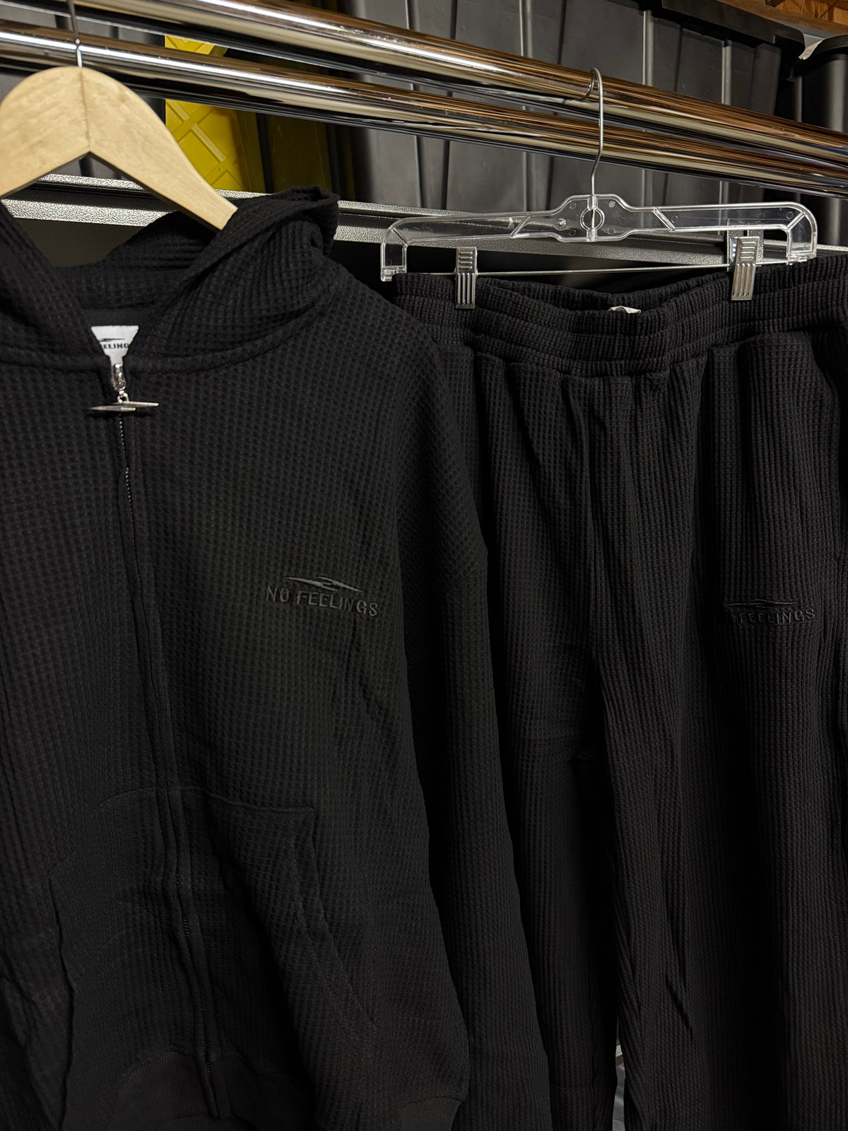 Closer view of the No Feelings black thermal set on a hanger, showing the ribbed texture, zip hardware and tonal logos