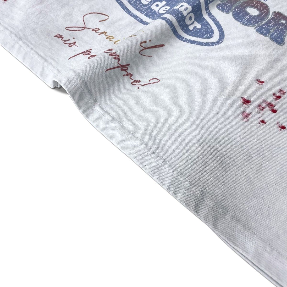 Stile De Amor White Buon Vino T-Shirt, angled view of the hem with the gold script reading Sarai tu il mio per sempre and red splatter across the white body