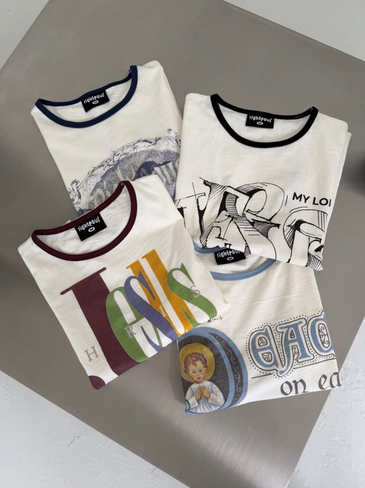 We Are Righteous ringer tees folded on a plinth showing assorted chest graphics