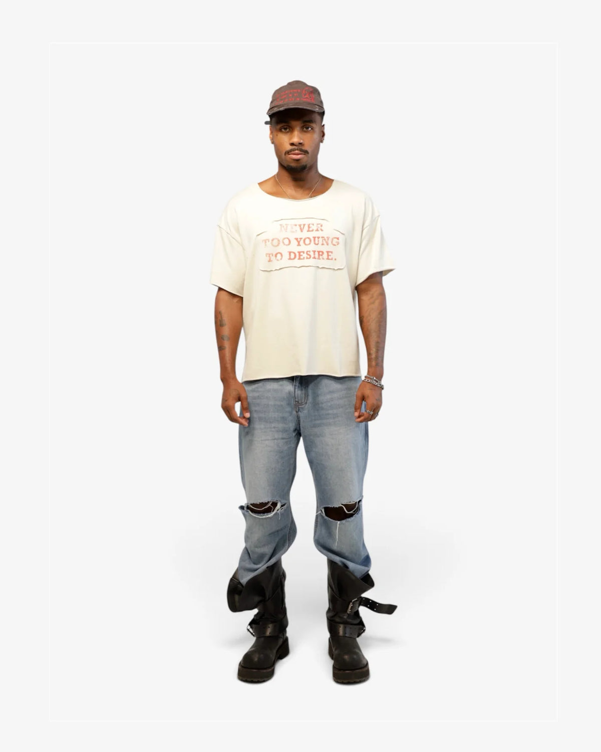 Male model in cream tee with blue ripped jeans and black boots, full length