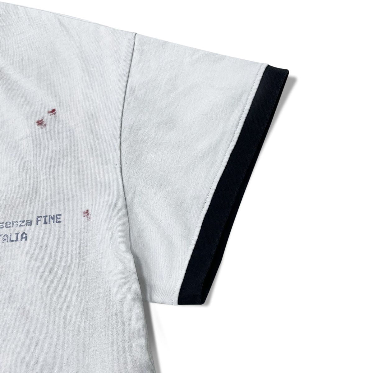 Stile De Amor White Buon Vino T-Shirt, close-up of the black ringer sleeve cuff with AMORE SENZA FINE ITALIA printed in navy beside red splatter on the white body