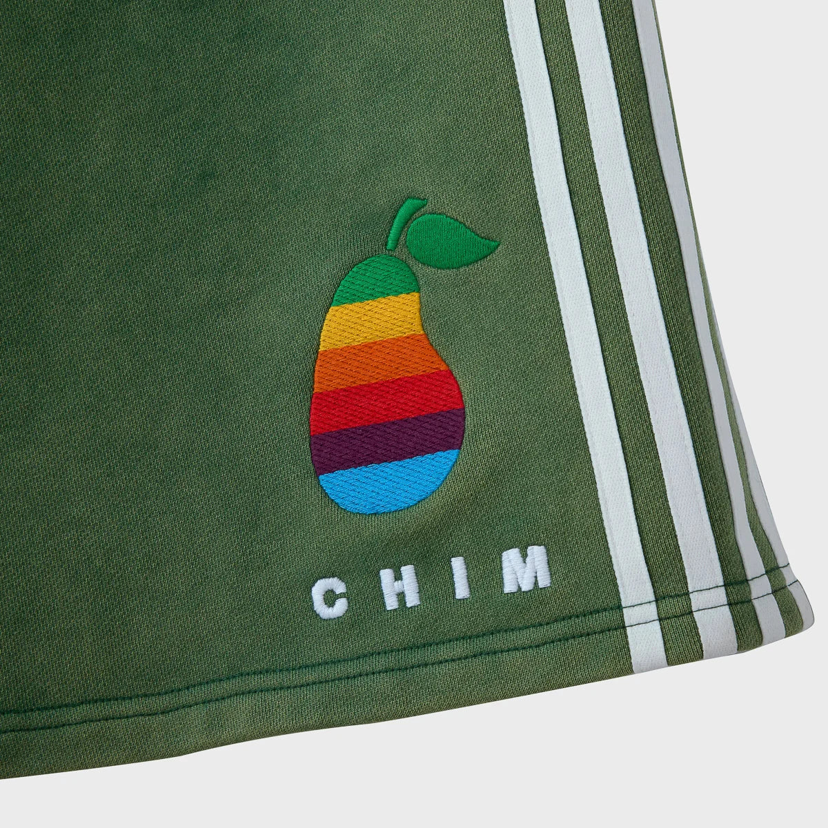Close-up of the rainbow-banded pear embroidery and white CHIM lettering above the topstitched hem, beside the three white side stripes
