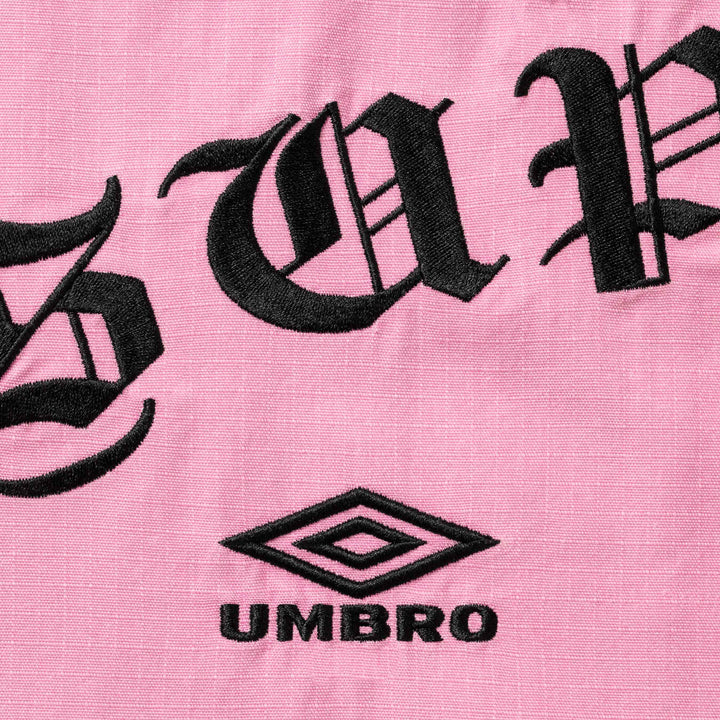 Close-up of black gothic lettering and the Umbro diamond logo embroidered on pink ripstop