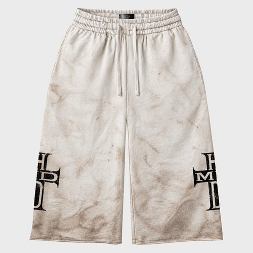 HMDD Holy Cross 3/4 shorts in off-white fleece with a brown mud-wash finish, drawcord waist and black HMDD cross graphics on the lower legs