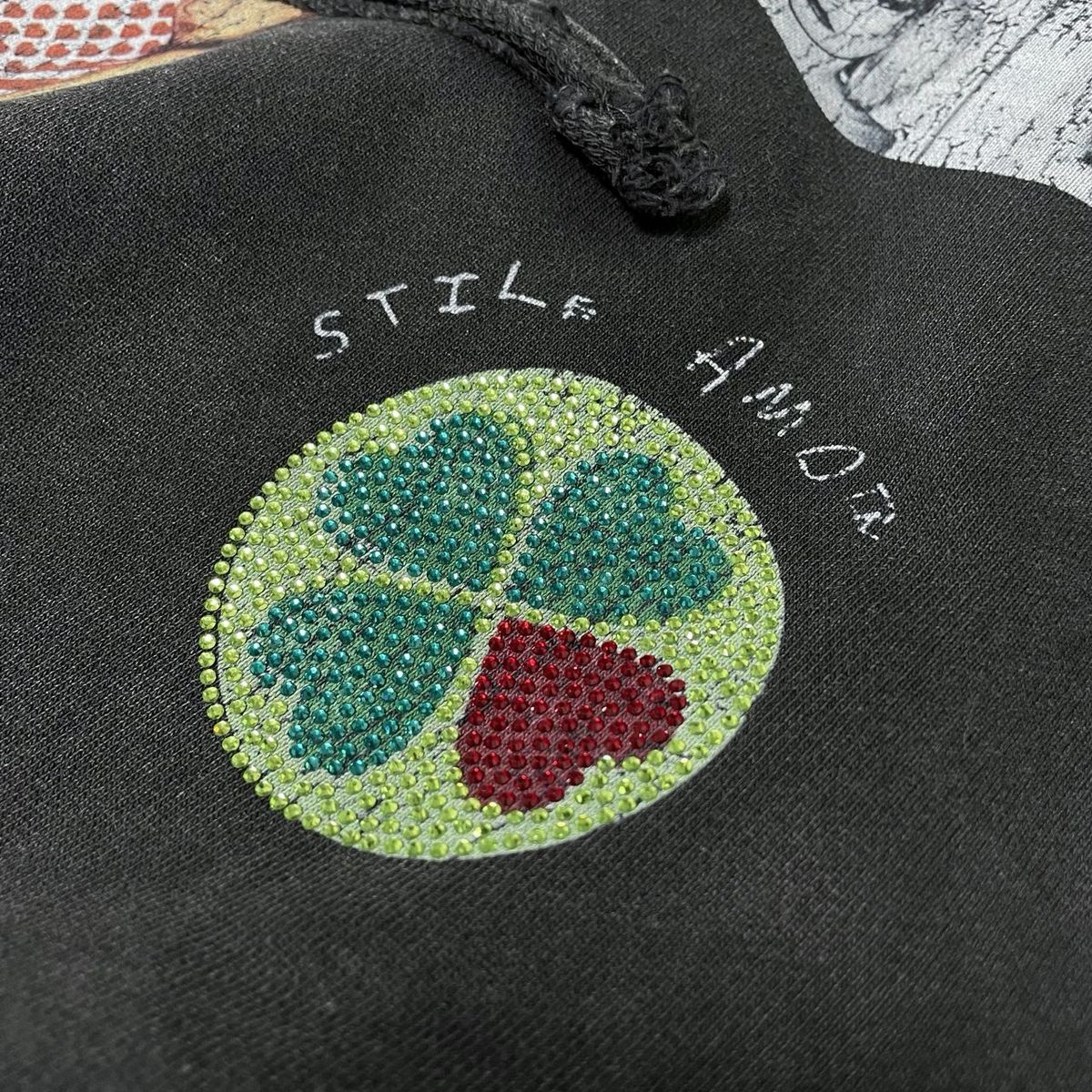 Close-up of the green and red rhinestone four-leaf clover on the Stile De Amor Sfera Hoodie