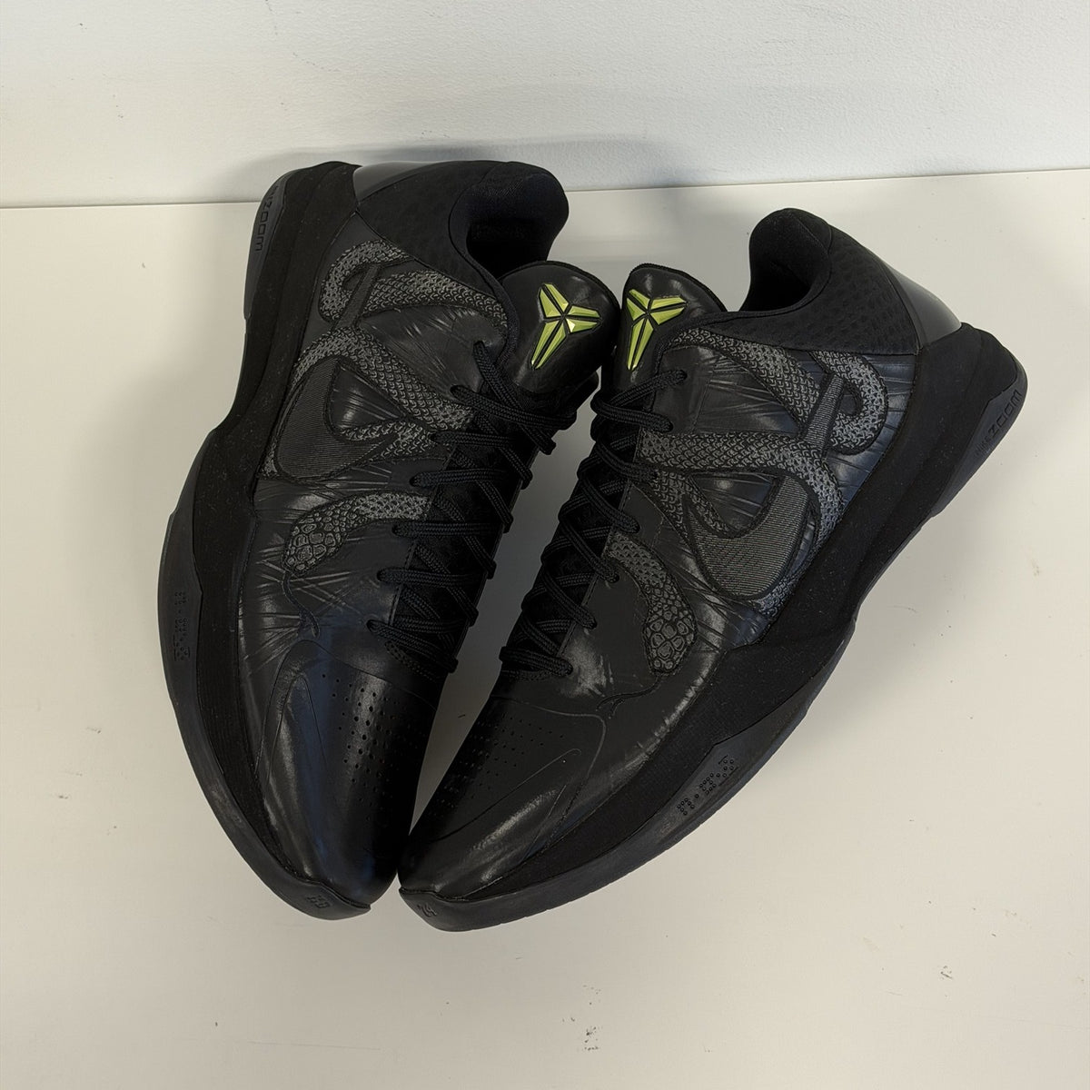 Nike Kobe 5 Protro Year of the Mamba Black, top-down view of both shoes showing the snake overlays and volt Kobe tongue logos